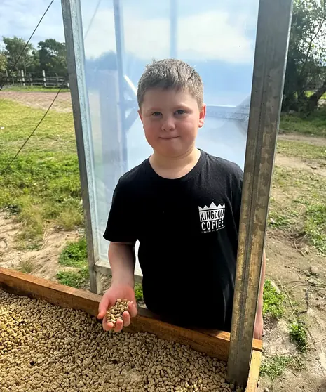 A boy holding a wooden tray of parchment coffee at the drying beds