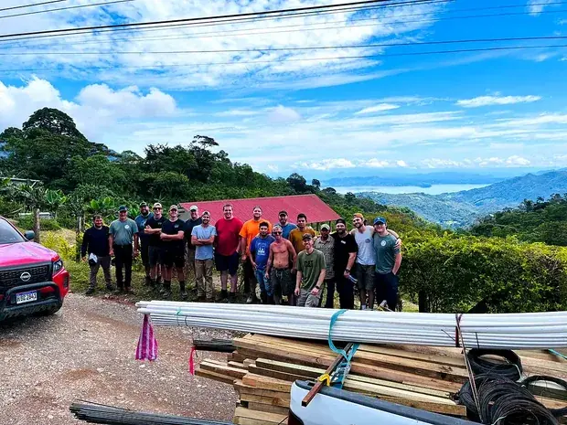 The visiting team and the farm crew on a hillside road, the valley and mountains behind them